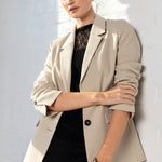 Woman wearing a beige blazer over a black top against a white wall.