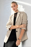 Woman wearing a beige blazer over a black top against a white wall.