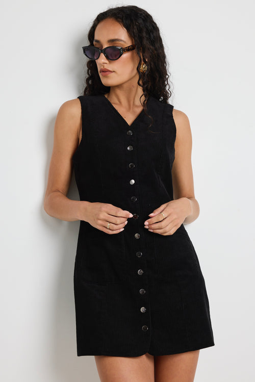 Model wears a black cord mini dress with silver buttons