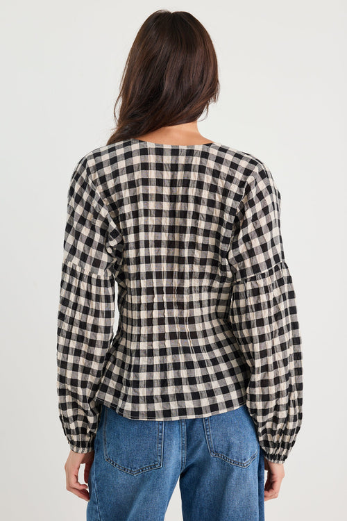 Person wearing a black and white checkered shirt and blue jeans on a plain background