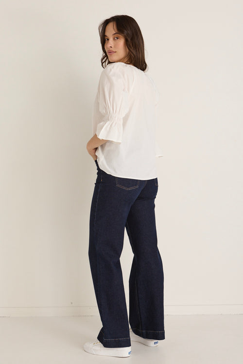 Model wears a white ruffle top with jeans