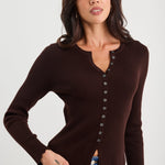 Woman wearing a brown ribbed long-sleeve top with buttons on a white background