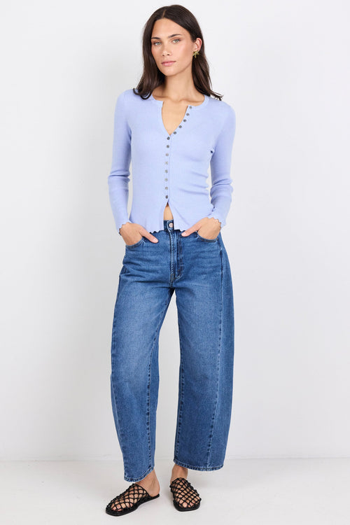 Woman wearing a light blue cardigan and blue jeans on a white background