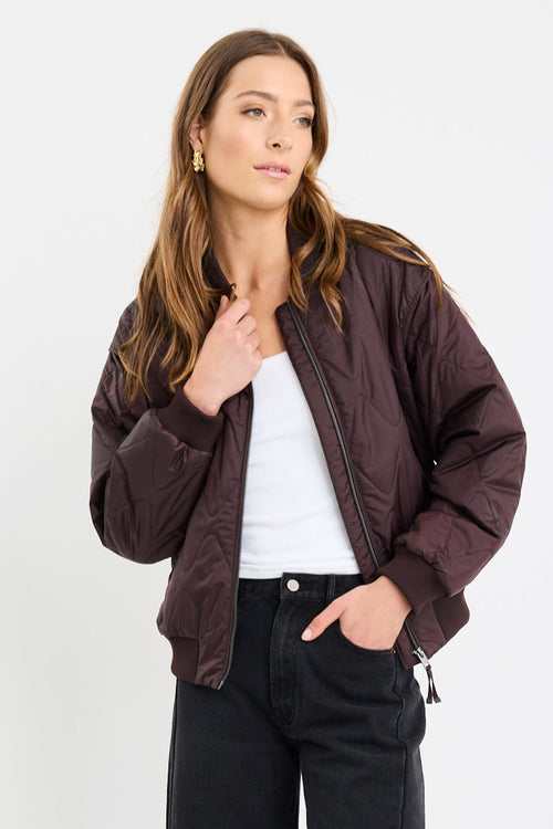Person wearing a brown jacket, white shirt, black pants, and black shoes on a white background