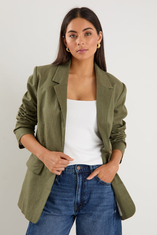 Model wears a green linen blazer with blue jeans