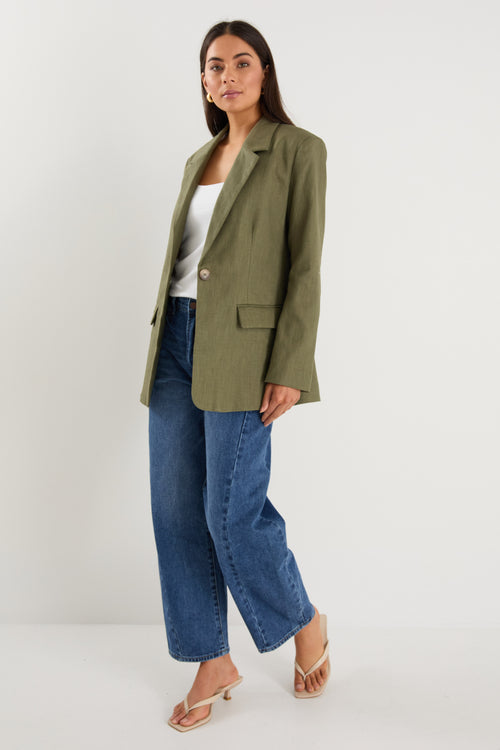 Woman wearing an olive green blazer and blue jeans on a white background