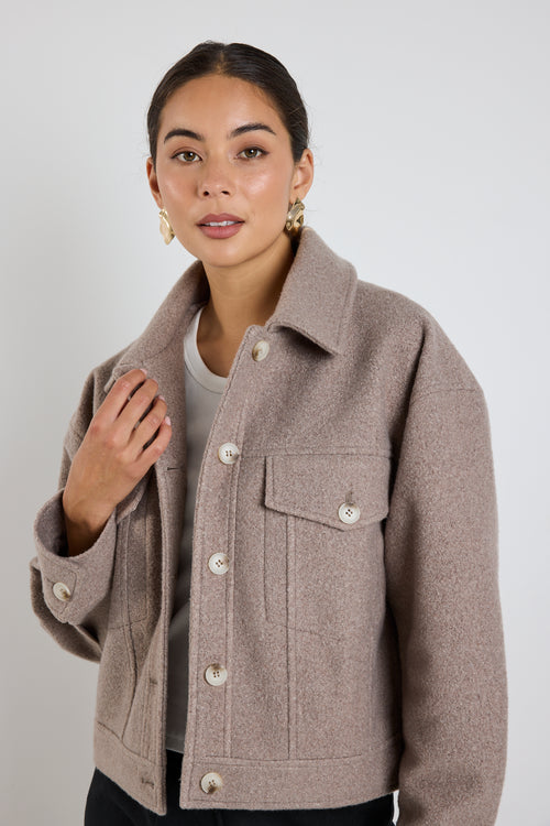 Woman wearing a taupe button-up trucker jacket with chest pockets and long sleeves, styled with a casual white top.
