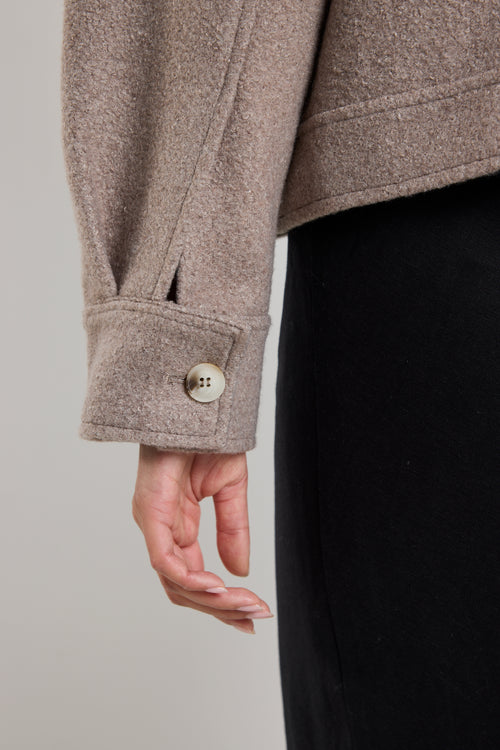 Woman wearing a taupe button-up trucker jacket with chest pockets and long sleeves, styled with a casual white top.