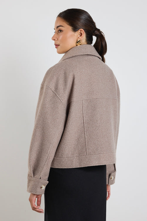 Woman wearing a taupe button-up trucker jacket with chest pockets and long sleeves, styled with a casual white top