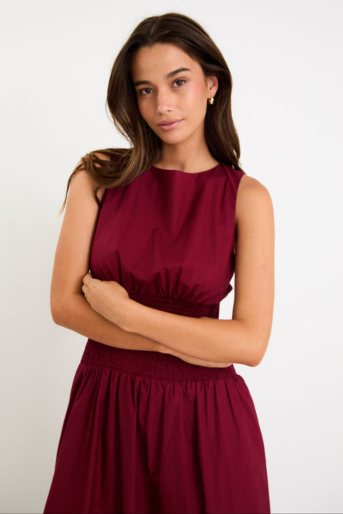 Model wearing a burgundy sleeveless maxi dress with a shirred waist and a flowing skirt.