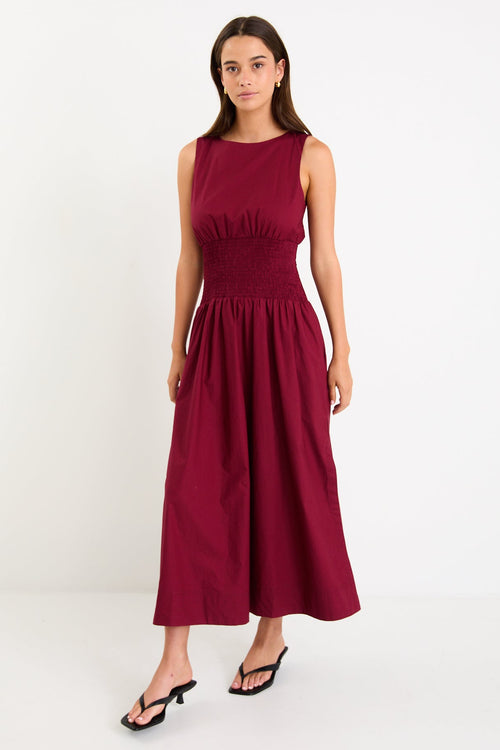 Model wearing a burgundy sleeveless maxi dress with a shirred waist and a flowing skirt.