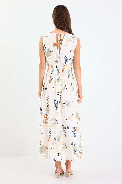 Woman wearing a sleeveless earthy botanical floral maxi dress with a shirred waist, tie detail, and a flattering, flowy silhouette.