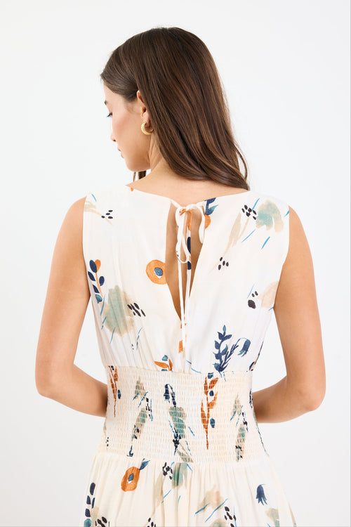 Woman wearing a sleeveless earthy botanical floral maxi dress with a shirred waist, tie detail, and a flattering, flowy silhouette.