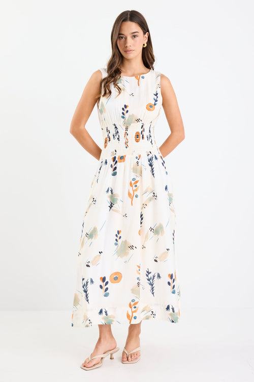 Woman wearing a sleeveless earthy botanical floral maxi dress with a shirred waist, tie detail, and a flattering, flowy silhouette.