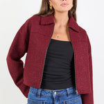 Woman wearing a maroon jacket, black top, and blue jeans on a white background