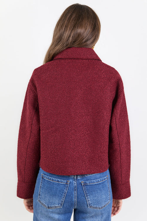 Person wearing a burgundy jacket and blue jeans on a white background