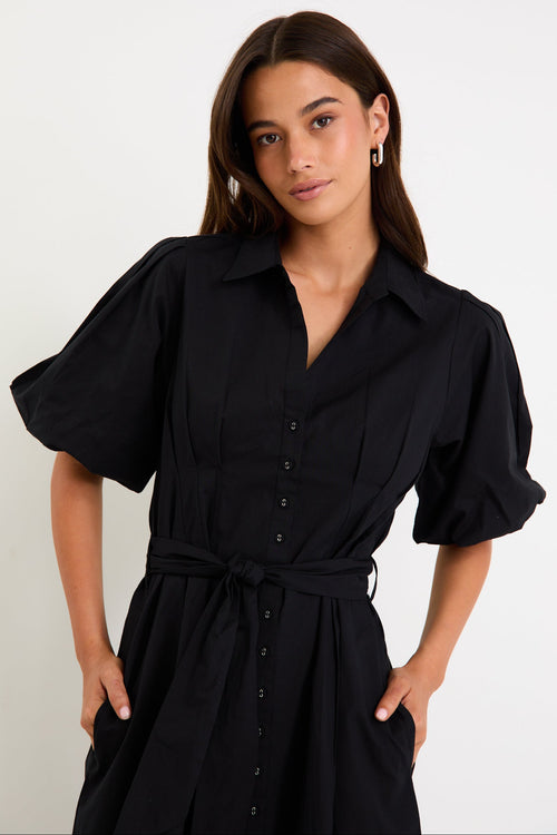 Woman wearing a black dress with puffed sleeves against a white background