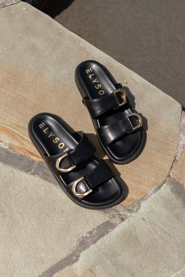 Black sandals with gold buckles on a stone surface