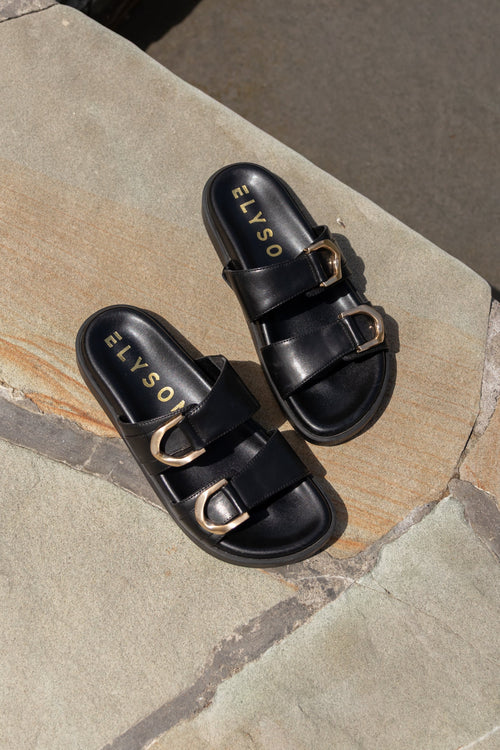 Black sandals with gold buckles on a stone surface