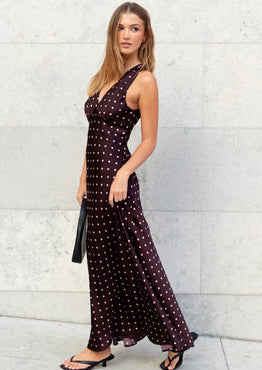 Woman in a dark dress with white polka dots standing against a light stone wall.