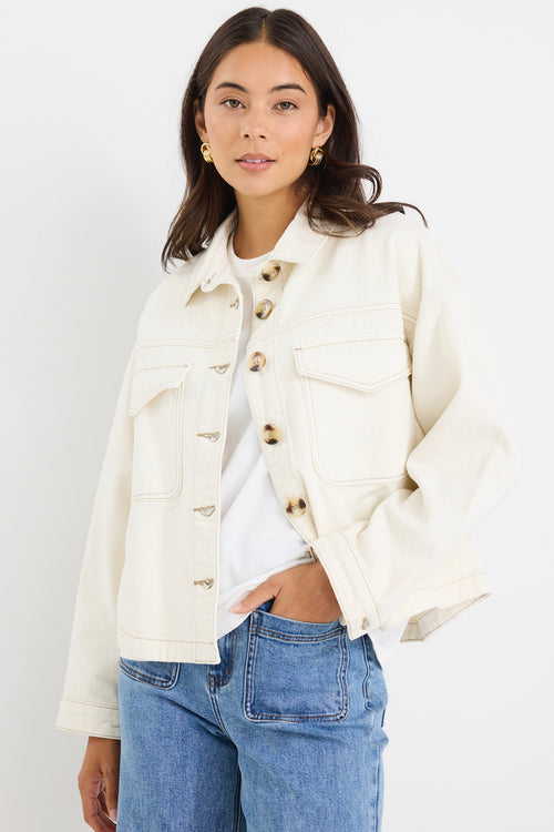 Woman wearing a relaxed fit off-white denim jacket with front flap pockets and tortoiseshell buttons, styled casually with jeans.