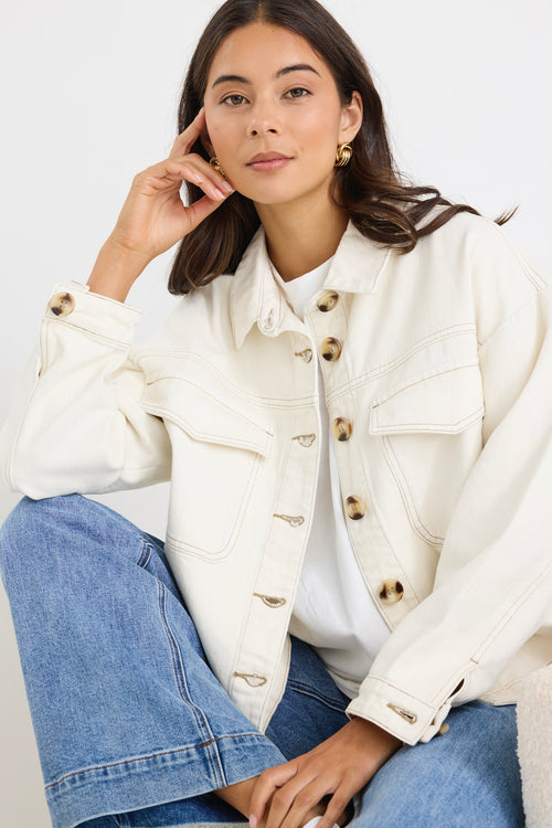 Woman wearing a relaxed fit off-white denim jacket with front flap pockets and tortoiseshell buttons, styled casually with jeans.
