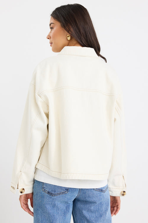 Woman wearing a relaxed fit off-white denim jacket with front flap pockets and tortoiseshell buttons, styled casually with jeans.