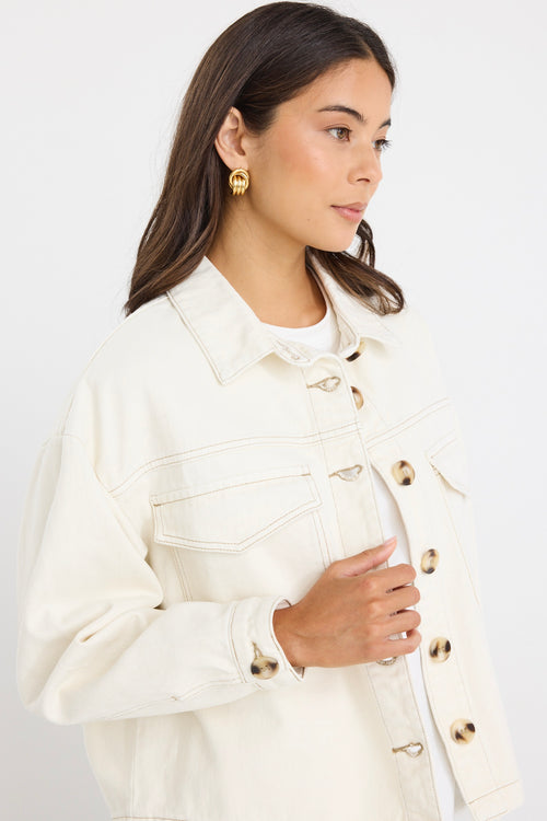 Woman wearing a relaxed fit off-white denim jacket with front flap pockets and tortoiseshell buttons, styled casually with jeans.