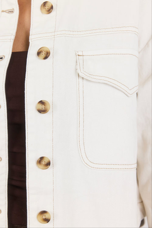 Close-up of a white denim jacket with gold buttons and a pocket.