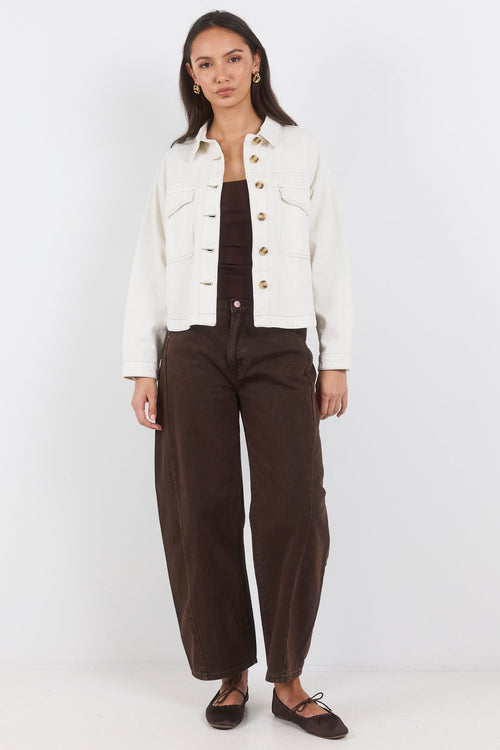 Woman wearing a white jacket, brown top, and dark pants on a white background