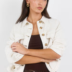 Woman wearing a white jacket with gold buttons on a plain background