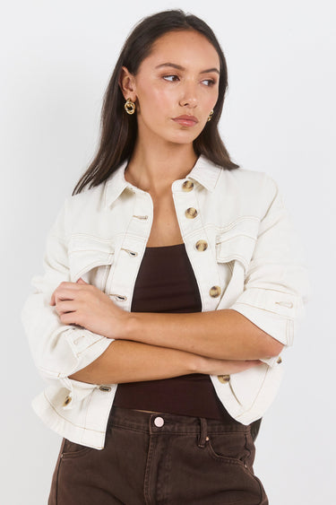 Woman wearing a white jacket with gold buttons on a plain background