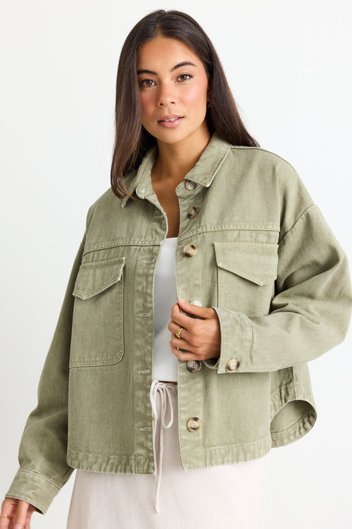 model wears a thick green cotton jacket over a white top and a beige linen skirt