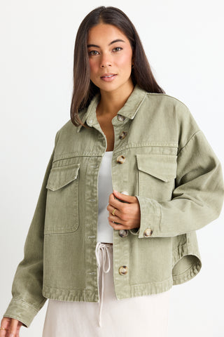 model wears a thick green cotton jacket over a white top and a beige linen skirt