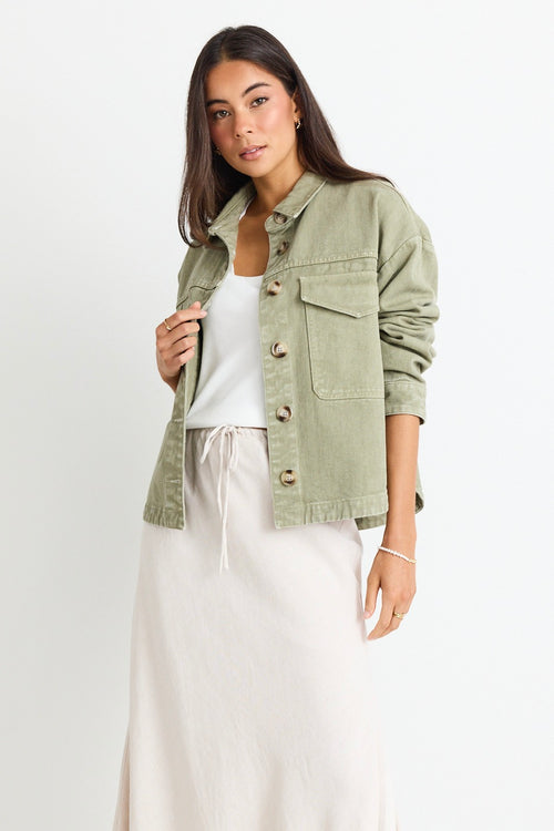 model wears a thick green cotton jacket over a white top and a beige linen skirt