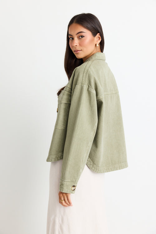 model wears a thick green cotton jacket over a white top and a beige linen skirt