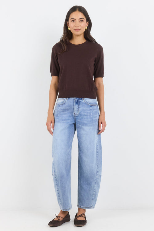Person wearing a brown t-shirt and light blue jeans on a white background