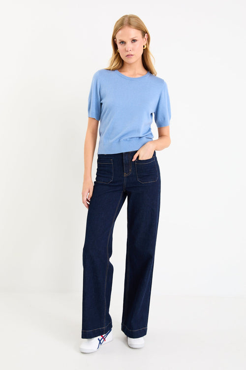 Model wearing a sky blue short sleeve crewneck knit tee tucked into dark denim