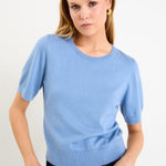 Model wearing a sky blue short sleeve crewneck knit tee tucked into dark denim