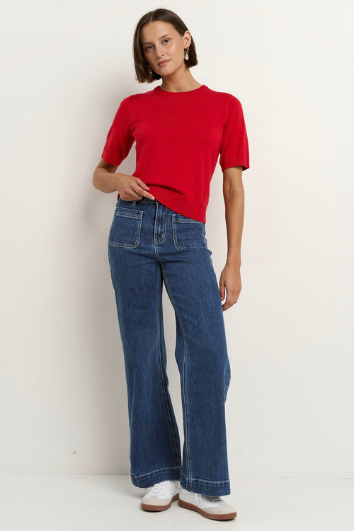 model wears a red knit t-shirt with dark blue wide leg jeans