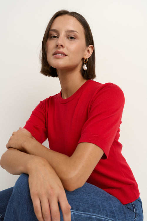 model wears a red knit t-shirt with dark blue wide leg jeans
