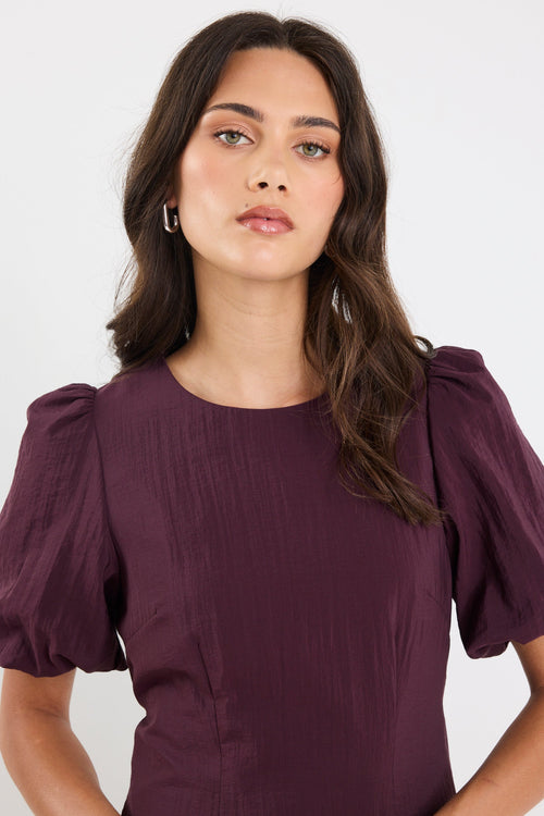 Woman wearing a purple dress with puffed sleeves against a white background