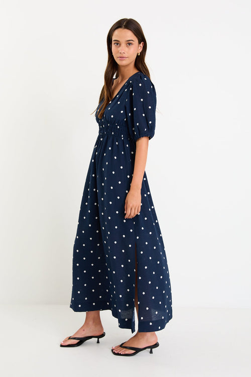 Model wearing a navy polka dot maxi dress with a V neckline, flutter sleeves and an elasticated waist
