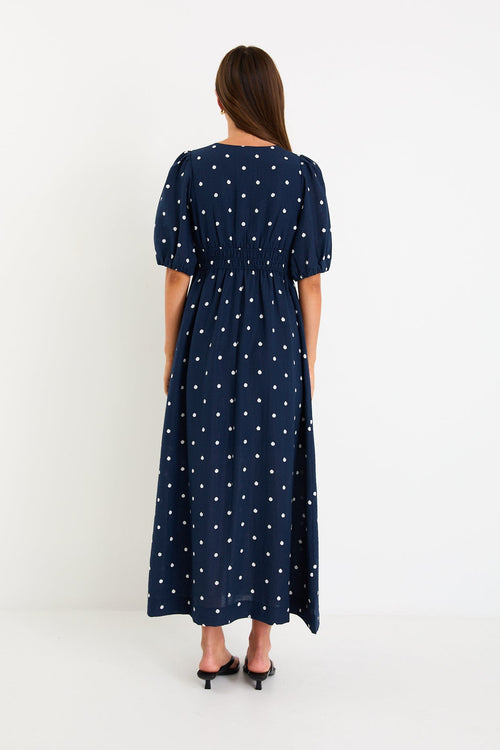 Model wearing a navy polka dot maxi dress with a V neckline, flutter sleeves and an elasticated waist