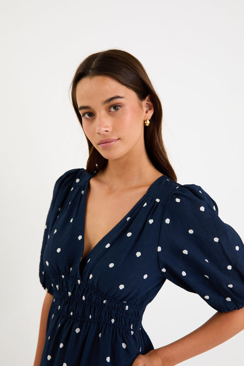 Model wearing a navy polka dot maxi dress with a V neckline, flutter sleeves and an elasticated waist