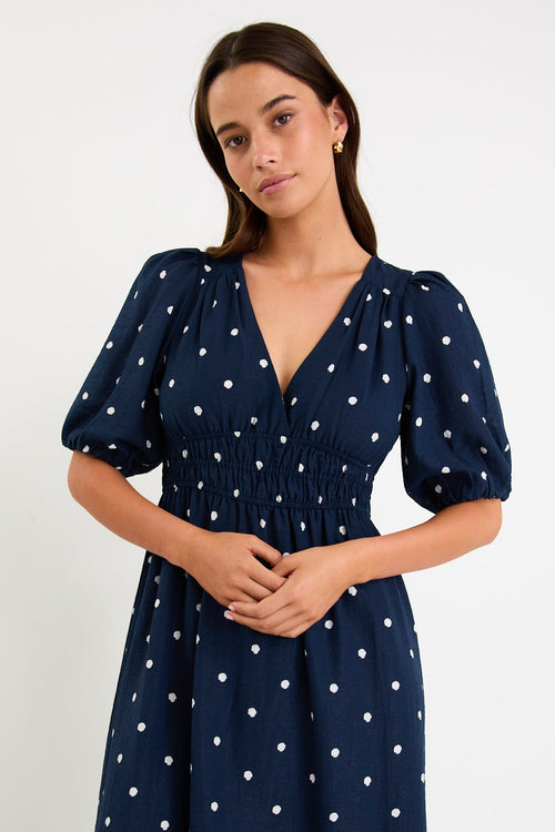 Woman wearing a navy dress with white polka dots against a plain background