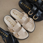 Elyson sandals in black, beige, and gold on a beige surface