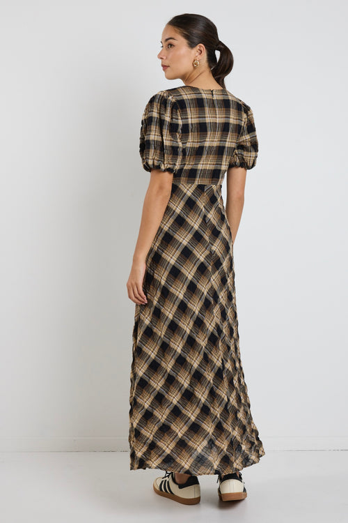 Woman wearing a caramel check maxi dress with balloon sleeves and flowing bias-cut skirt, styled with casual sneakers.