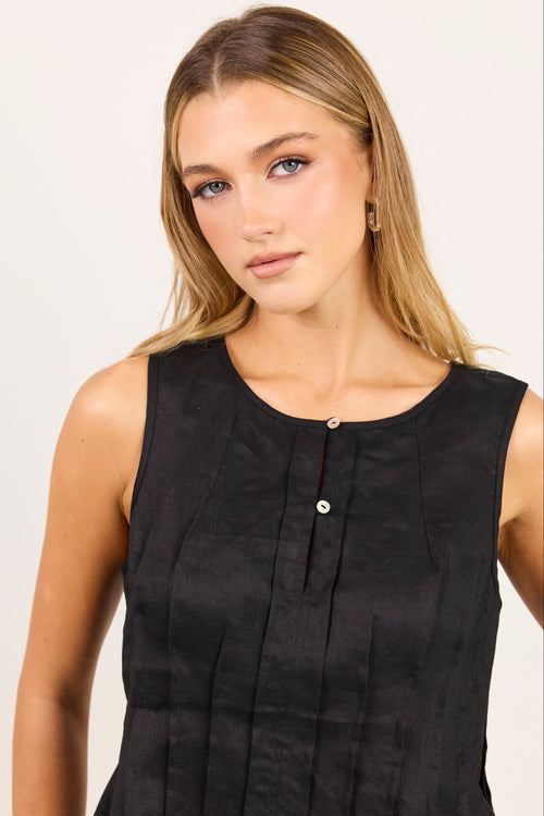 A woman modeling a sleeveless black top with a round neckline and a small button detail at the center front, set against a plain light background.