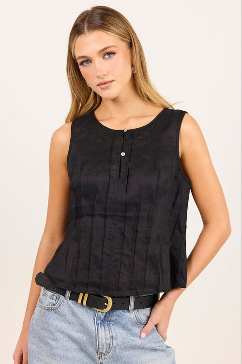 A woman modeling a sleeveless black top with a gathered peplum-like waist and a small decorative button at the neckline, paired with light blue jeans and a black belt, against a plain light background.